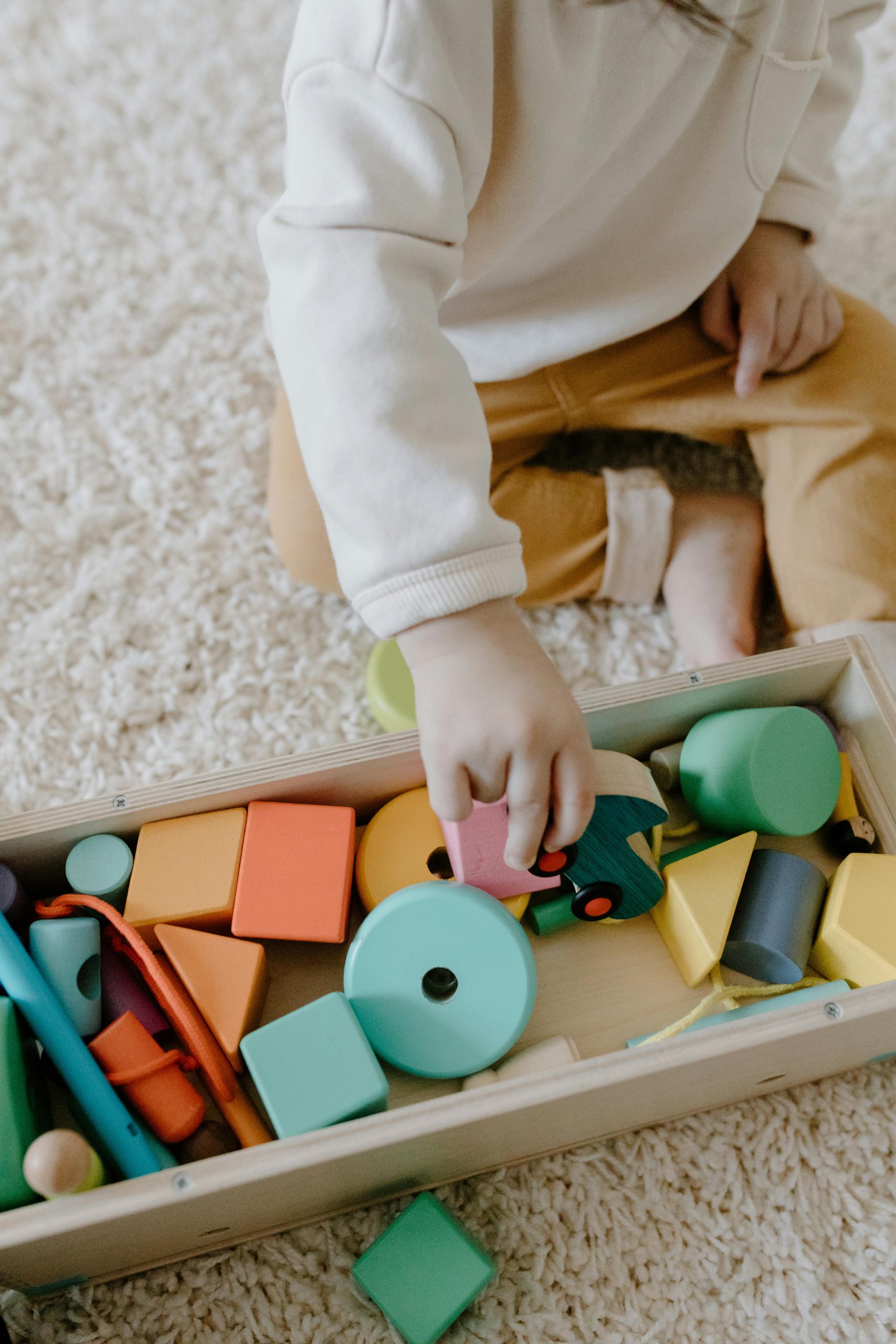 Child playing with vibrant wooden blocks on carpet, enhancing learning through play.